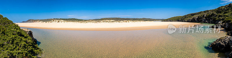 在一个阳光明媚的日子里，这张超广角全景照片捕捉到了清澈的Ribeira de Aljezur河、沙滩、沙丘和宽阔的海滩，展示了葡萄牙美丽的自然风光。